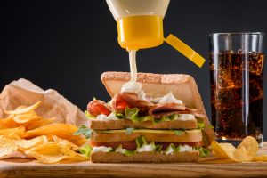 Pouring mayonnaise on sandwich with meat, cheese and vegetables